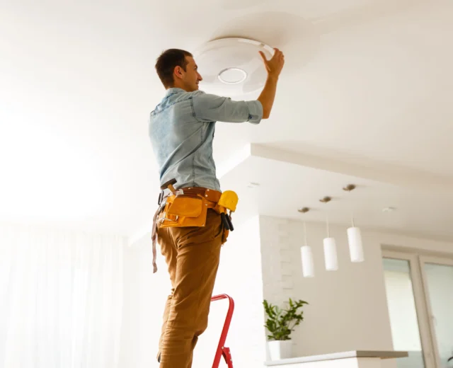 Electrician installing a light fixture in a residential home.