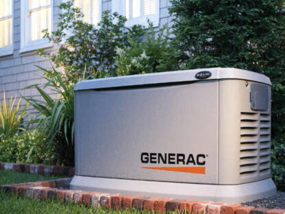 A Generac generator installed outside a house on a brick platform, surrounded by grass and small shrubs.