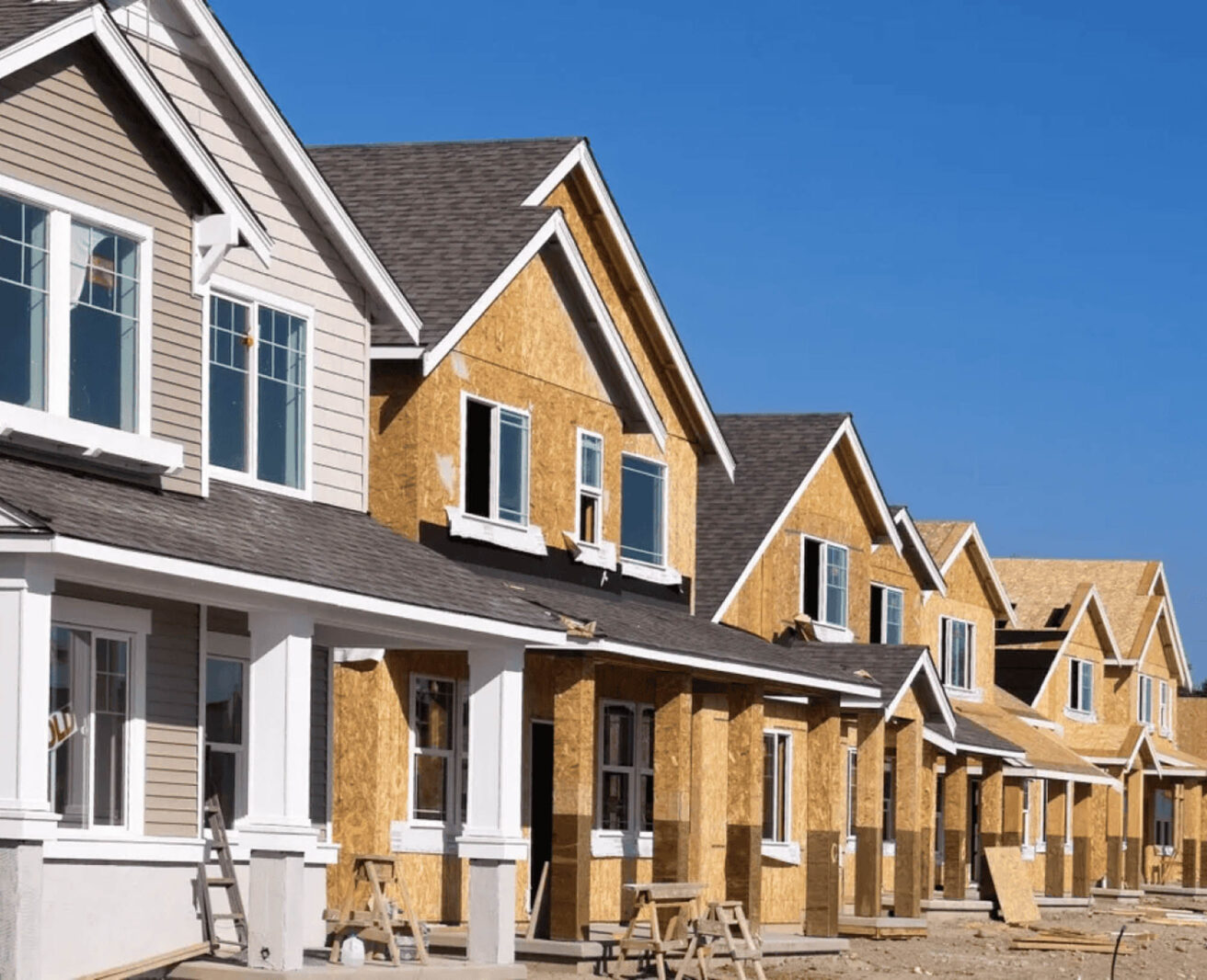 Row of houses under construction with wooden frames, windows, and partially completed exteriors under a clear blue sky in Central Florida.