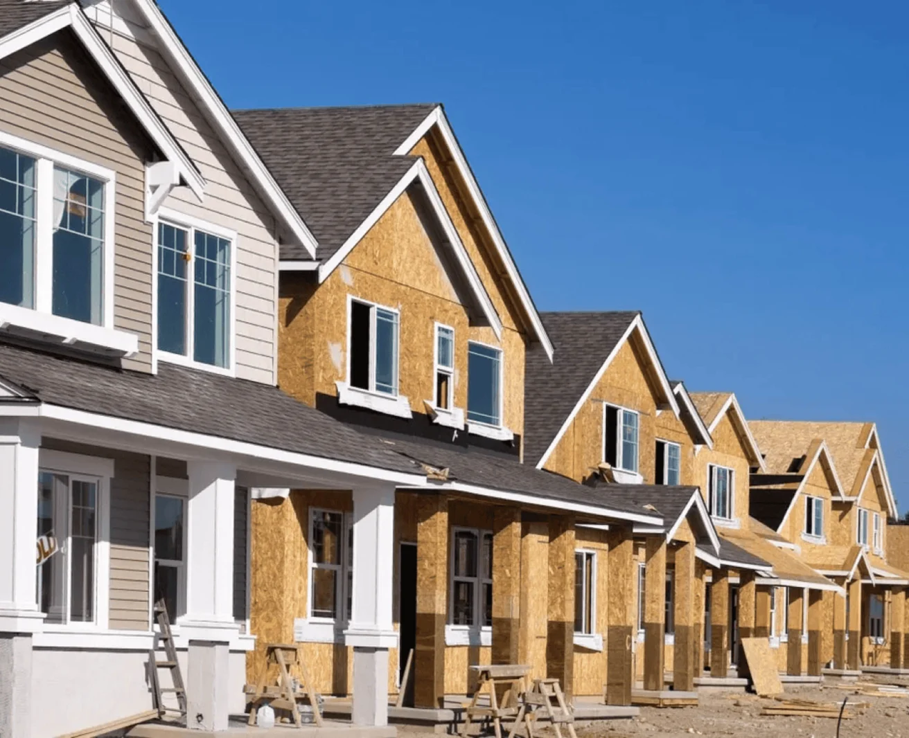 Row of houses under construction with wooden frames, windows, and partially completed exteriors under a clear blue sky in Central Florida.