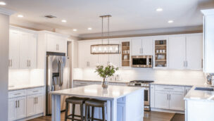 Modern kitchen with white cabinets, stainless steel appliances, a large island with two stools, and recessed lighting.