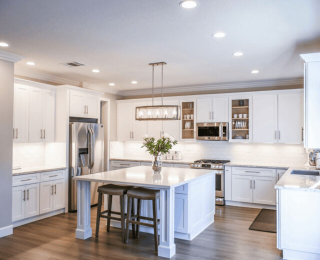 Modern kitchen with white cabinets, stainless steel appliances, a large island with two stools, and recessed lighting.