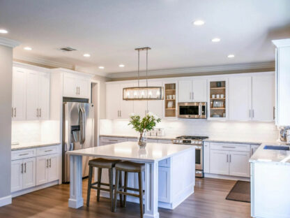 Modern kitchen with white cabinets, stainless steel appliances, a central island with two stools, and recessed lighting. A vase with flowers is on the island.