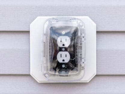 Outdoor electrical outlet with cover mounted on a vinyl siding wall.