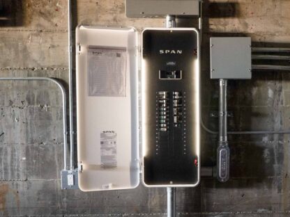An open electrical panel attached to a wall with labeled switches and wiring visible.|Person adjusting a smart thermostat using a smartphone app. Both devices display a temperature of 77°F.|