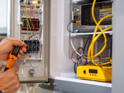A person uses a handheld device to test wires in an electrical panel box||with various tools and a yellow voltmeter displayed.