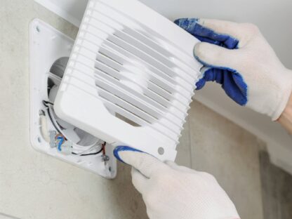 Person wearing gloves installs a white vent cover on a wall.|Modern bathroom with a glass shower enclosure|