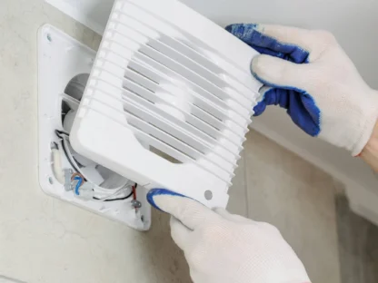 Person wearing gloves installs a white vent cover on a wall.|Modern bathroom with a glass shower enclosure|