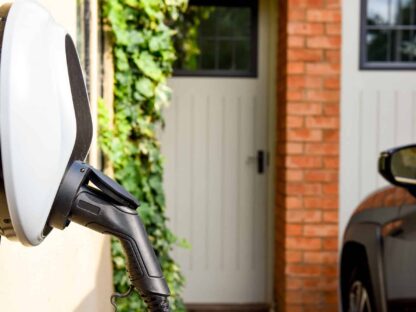 Premium EV Outlet plugged into the wall of a house to charge an electric car.||