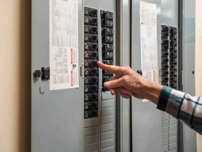 A person adjusts a breaker switch inside an open electrical panel mounted on a wall.|Male electrician turning off power for electrical outlet at circuit breaker box. Resetting tripped breaker in residential electricity power panel.|