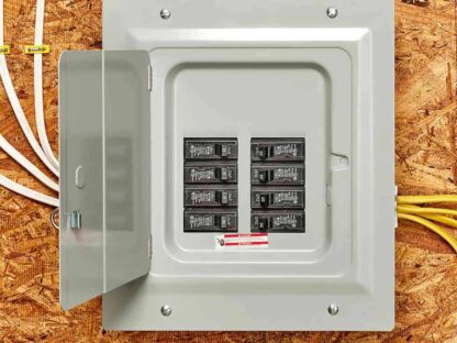 An open electrical panel with circuit breakers mounted on a plywood wall|