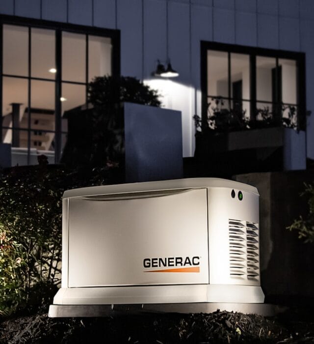 Generac generator installed with outdoor lighting illuminating the appliance at night.